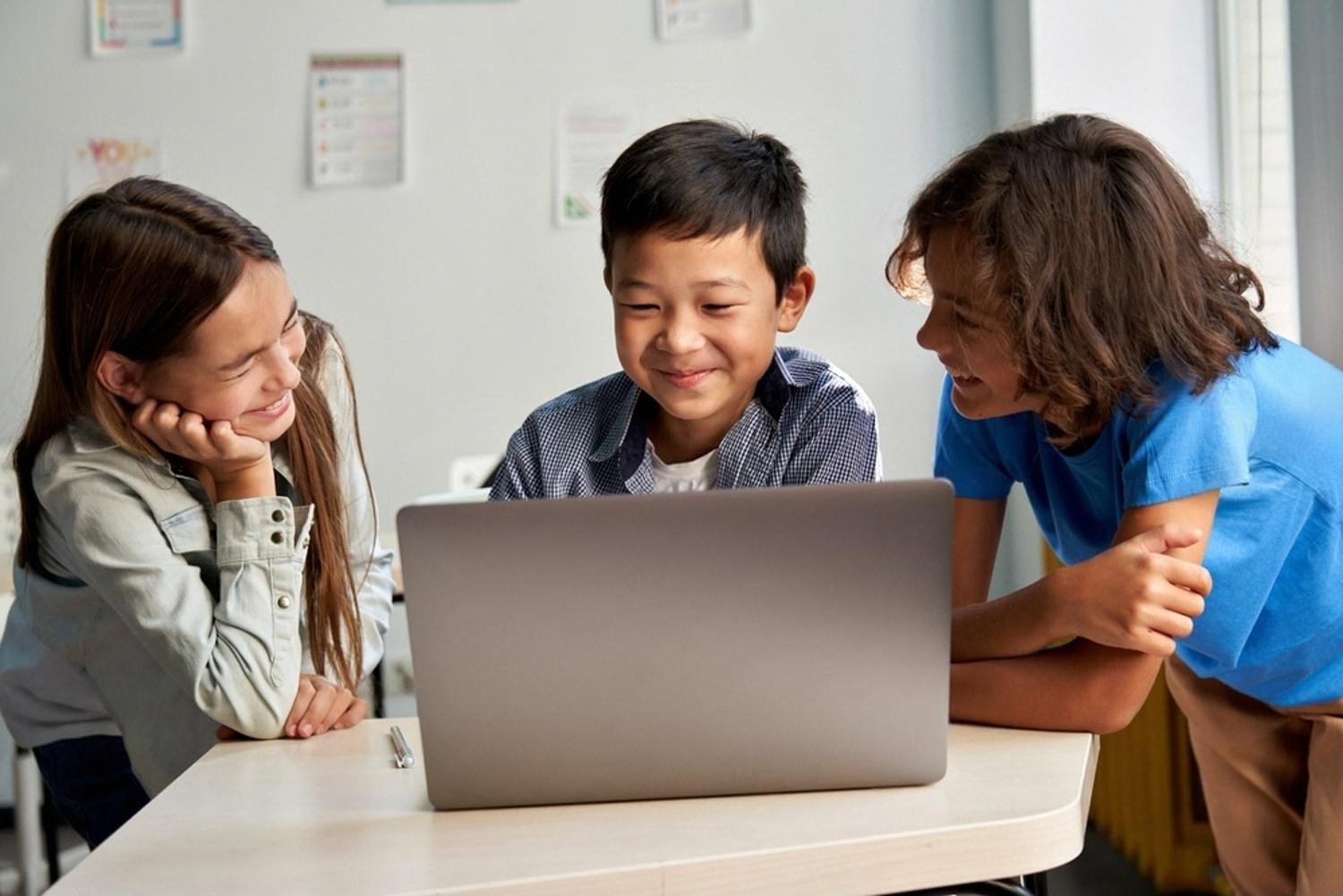 Three young students working together on a laptop during a classroom project
